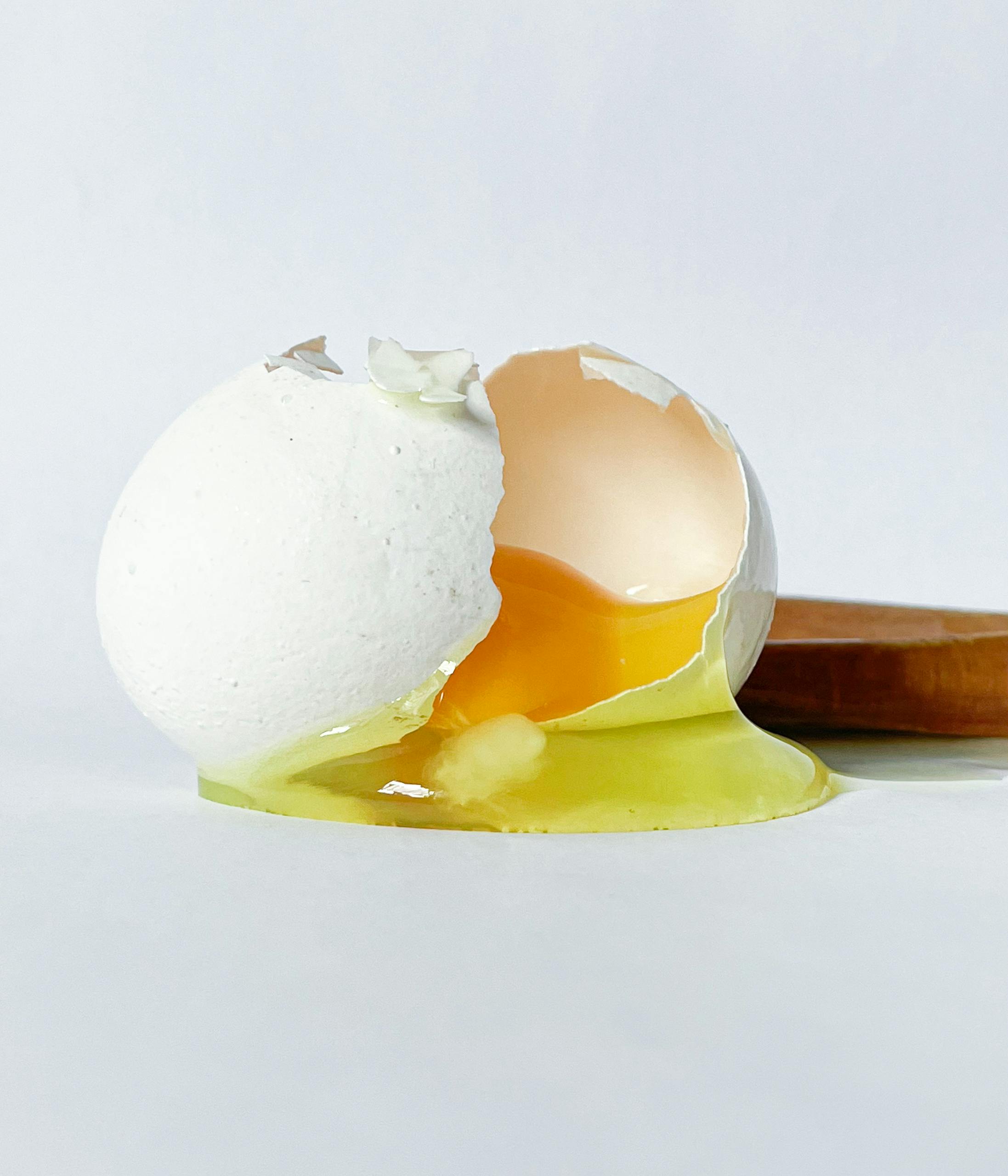 A close-up of a cracked egg with yolk spilling out, highlighting freshness.