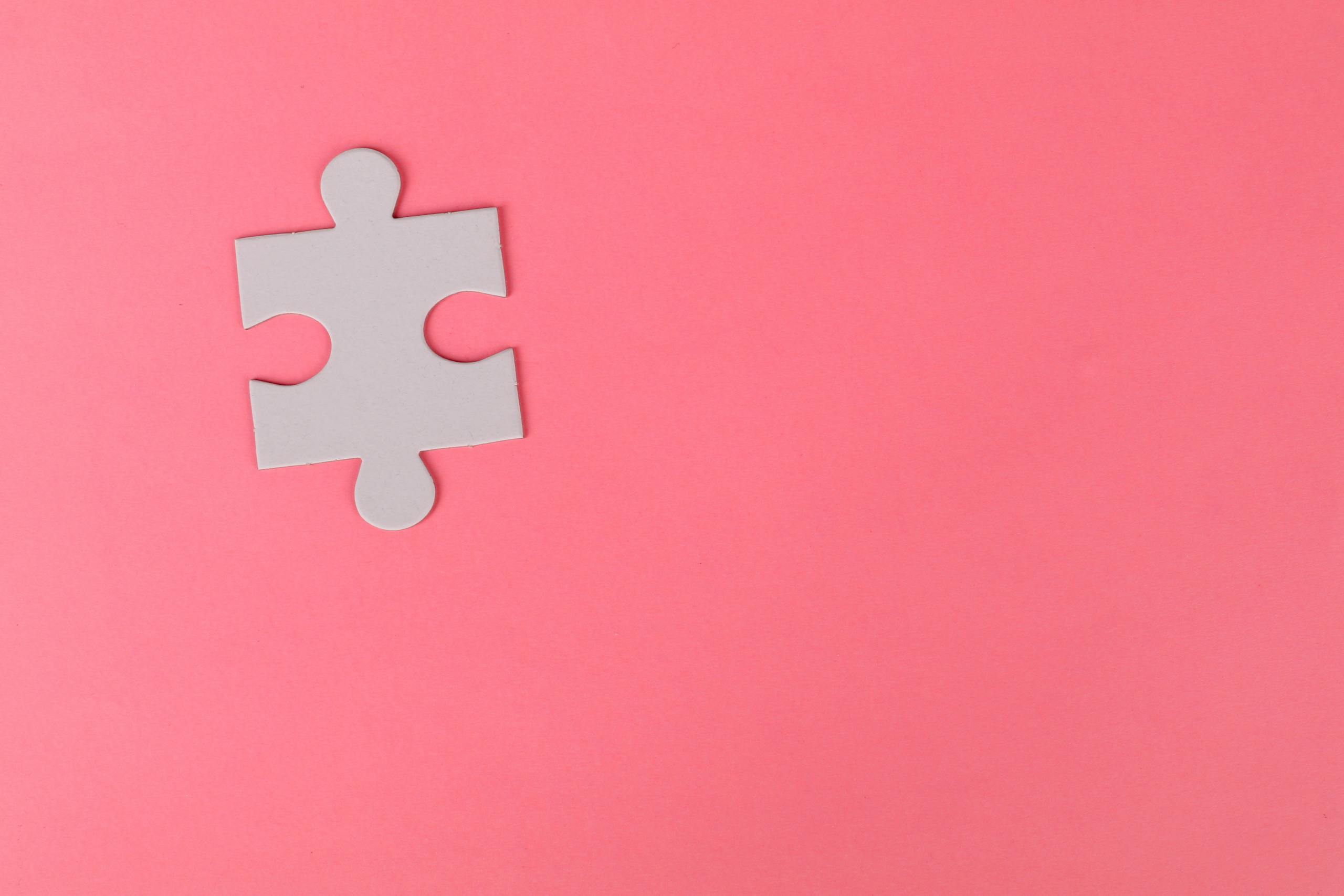 A single puzzle piece set against a vibrant pink background, offering ample copy space.