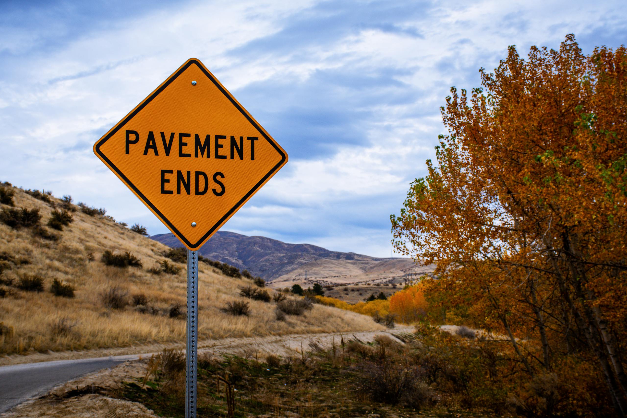 Autumn landscape featuring a 'Pavement Ends' sign along a rural road.