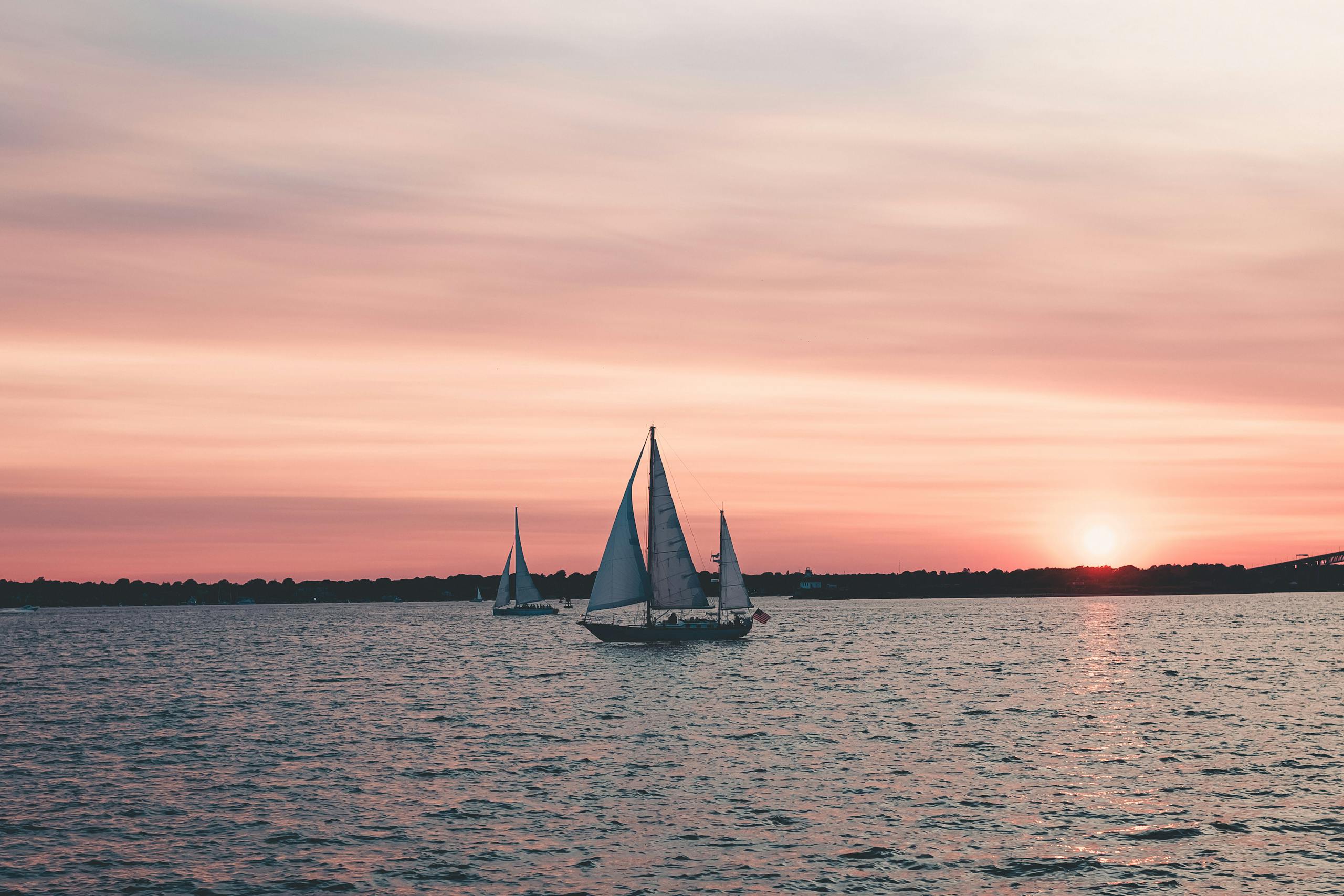 Beautiful sunset view of sailboats gliding on the ocean with a vibrant sky.