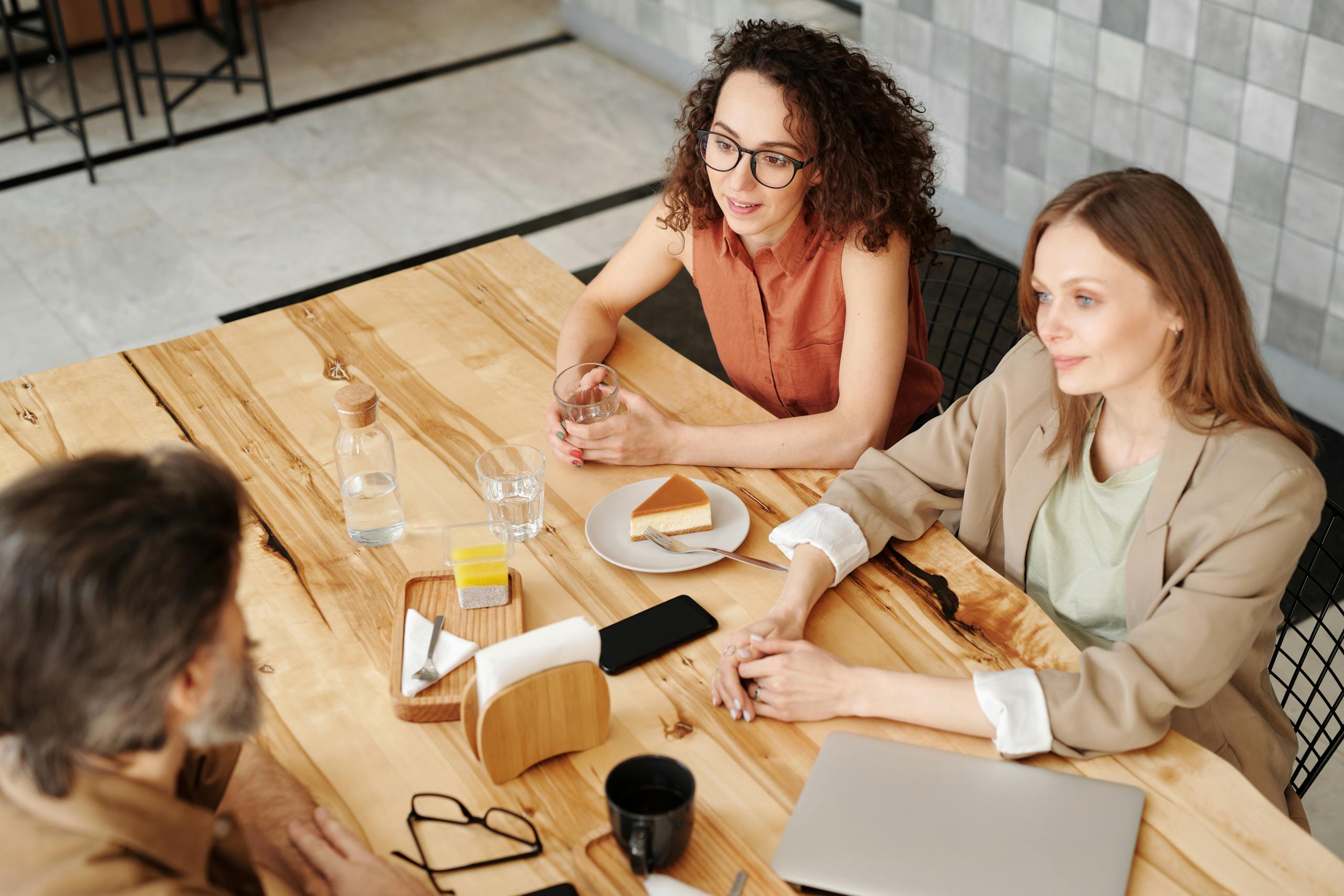 Three adults in a relaxed business meeting enjoying coffee and cake at a wooden table.